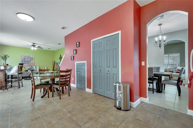 dining area with ceiling fan with notable chandelier, a textured ceiling, and tile patterned floors