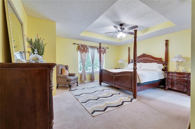 bedroom featuring a textured ceiling, a tray ceiling, ceiling fan, and light colored carpet