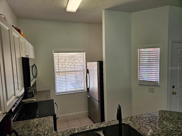 kitchen featuring a textured ceiling, appliances with stainless steel finishes, light tile patterned flooring, and white cabinetry