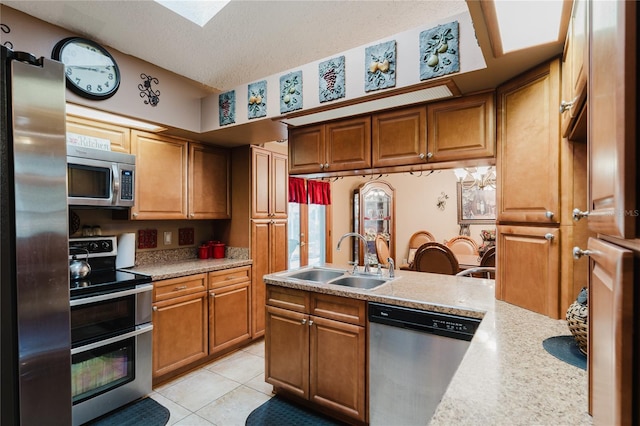 kitchen featuring appliances with stainless steel finishes, light tile patterned floors, a textured ceiling, a skylight, and sink