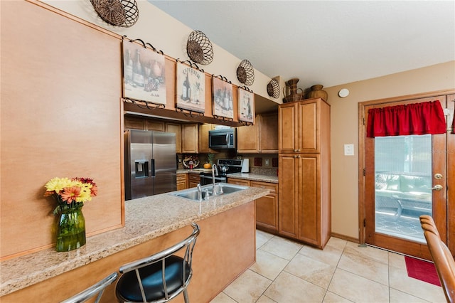 kitchen with appliances with stainless steel finishes, light tile patterned flooring, light stone counters, kitchen peninsula, and sink