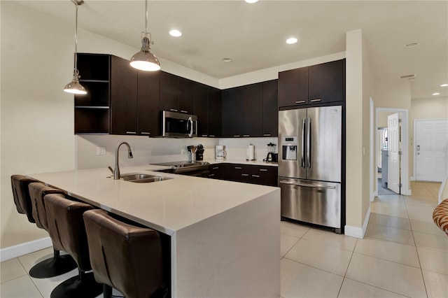 kitchen with hanging light fixtures, sink, kitchen peninsula, dark brown cabinets, and stainless steel appliances