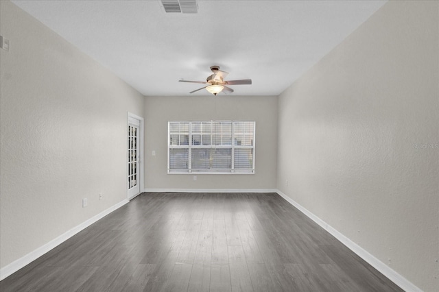 empty room featuring baseboards, visible vents, ceiling fan, and dark wood-style flooring