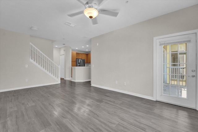 unfurnished living room with baseboards, stairway, a ceiling fan, and dark wood-style flooring