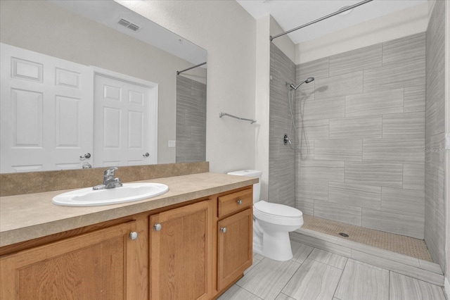 bathroom featuring vanity, toilet, a tile shower, and tile patterned flooring