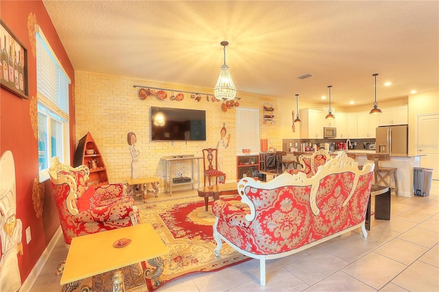 living room with a notable chandelier, light tile patterned floors, a textured ceiling, and brick wall