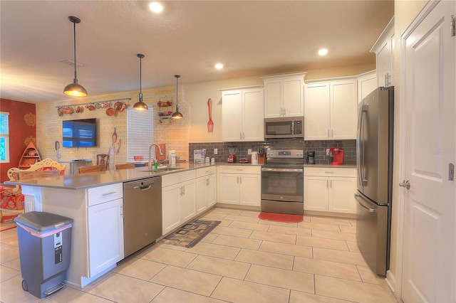 kitchen with kitchen peninsula, appliances with stainless steel finishes, sink, white cabinets, and hanging light fixtures