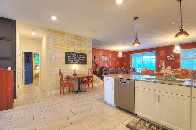 kitchen featuring dishwasher, sink, brick wall, decorative light fixtures, and white cabinets