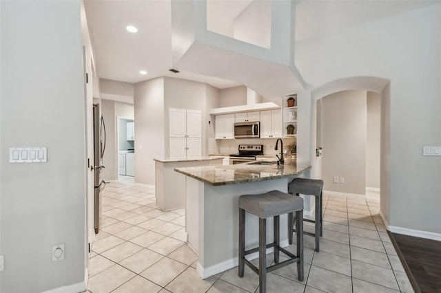 kitchen featuring appliances with stainless steel finishes, white cabinetry, kitchen peninsula, stone counters, and sink