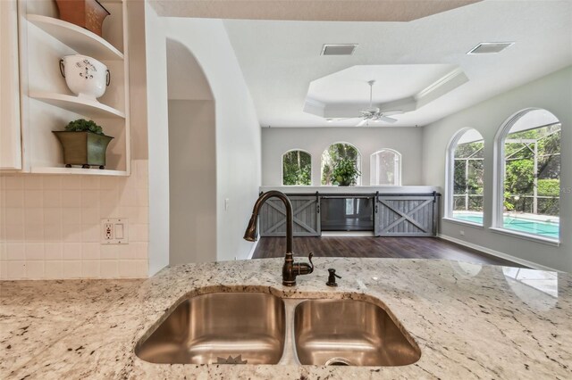 kitchen featuring light stone counters, a tray ceiling, ceiling fan, hardwood / wood-style floors, and sink