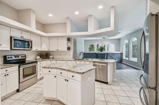 kitchen with sink, white cabinets, kitchen peninsula, a kitchen island, and appliances with stainless steel finishes