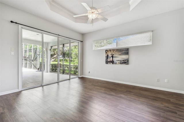 empty room with ceiling fan, a raised ceiling, and dark hardwood / wood-style flooring