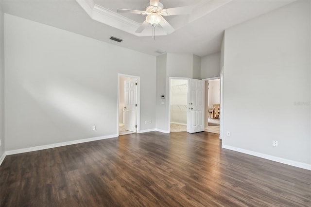 unfurnished bedroom with a tray ceiling, a closet, a walk in closet, dark hardwood / wood-style flooring, and ceiling fan