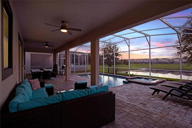 patio terrace at dusk featuring ceiling fan, a lanai, an outdoor living space, a swimming pool with hot tub, and a water view