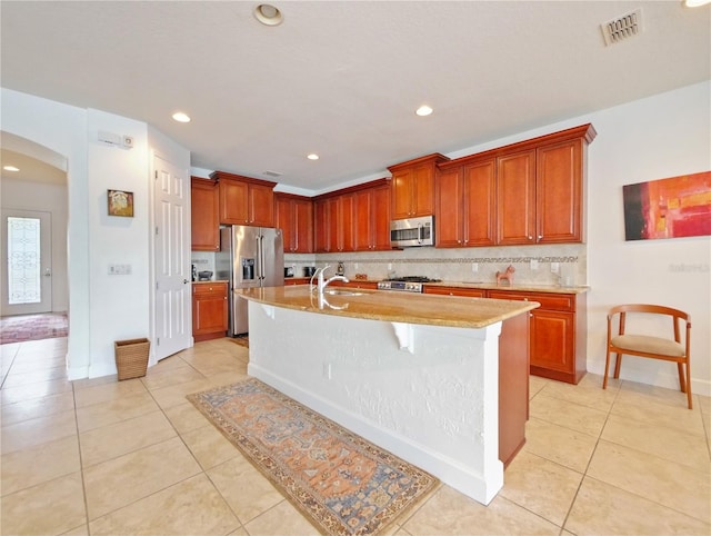 kitchen with an island with sink, appliances with stainless steel finishes, light tile patterned floors, and a breakfast bar area