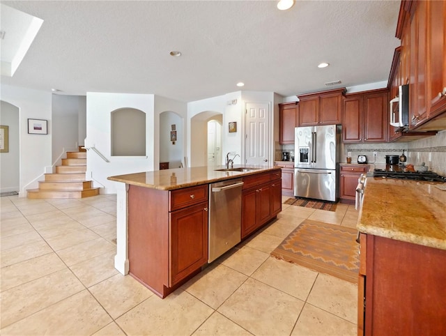 kitchen with light tile patterned floors, sink, a kitchen island with sink, backsplash, and appliances with stainless steel finishes