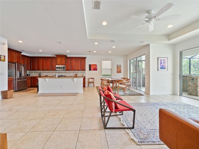 kitchen with appliances with stainless steel finishes, light tile patterned floors, a kitchen island with sink, and ceiling fan