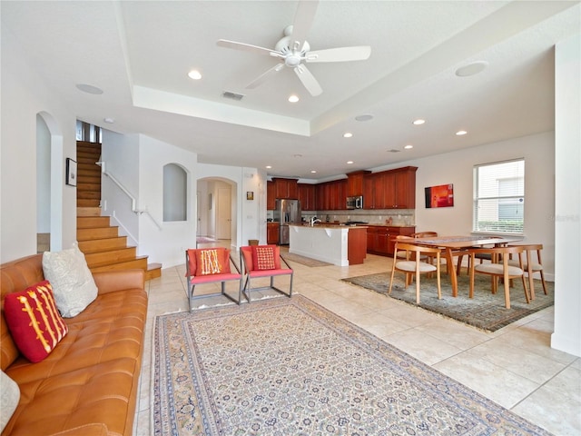 living room featuring ceiling fan, light tile patterned flooring, and a tray ceiling