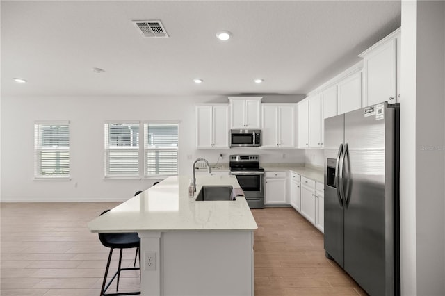 kitchen with appliances with stainless steel finishes, a center island with sink, white cabinetry, and light hardwood / wood-style flooring