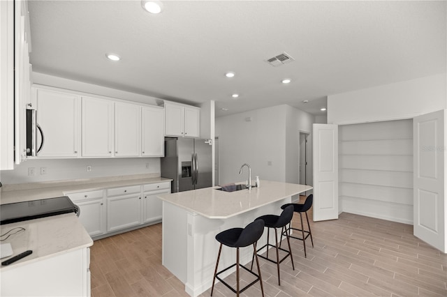 kitchen with white cabinets, sink, a center island with sink, light hardwood / wood-style flooring, and appliances with stainless steel finishes