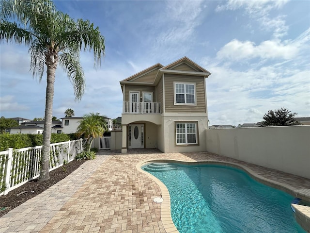 back of property with a balcony, a patio, and a fenced in pool