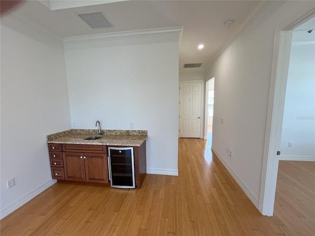 bar featuring light wood-type flooring, crown molding, beverage cooler, and sink