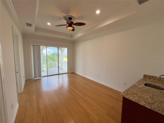 interior space with a tray ceiling, light hardwood / wood-style floors, crown molding, and sink