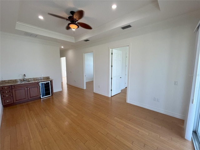 unfurnished living room with beverage cooler, a tray ceiling, light wood-type flooring, and ornamental molding