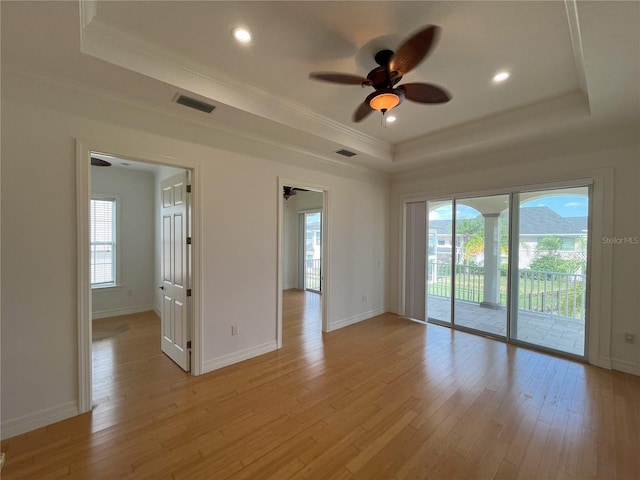 spare room featuring a healthy amount of sunlight, light hardwood / wood-style floors, a tray ceiling, and ceiling fan