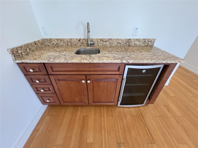 bar with light stone countertops, beverage cooler, light wood-type flooring, and sink