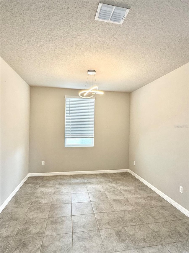 empty room with an inviting chandelier, tile patterned flooring, and a textured ceiling