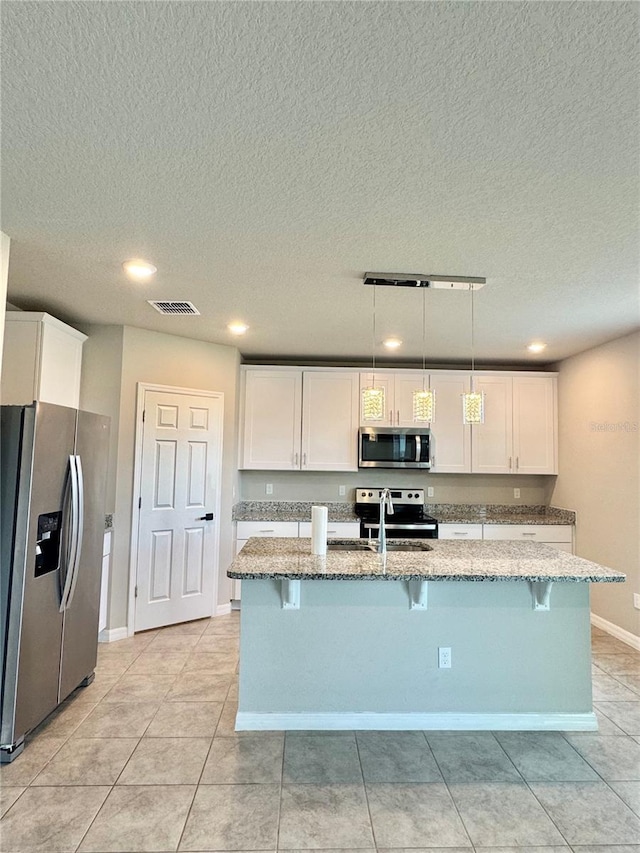 kitchen with pendant lighting, white cabinetry, stainless steel appliances, and a kitchen island with sink