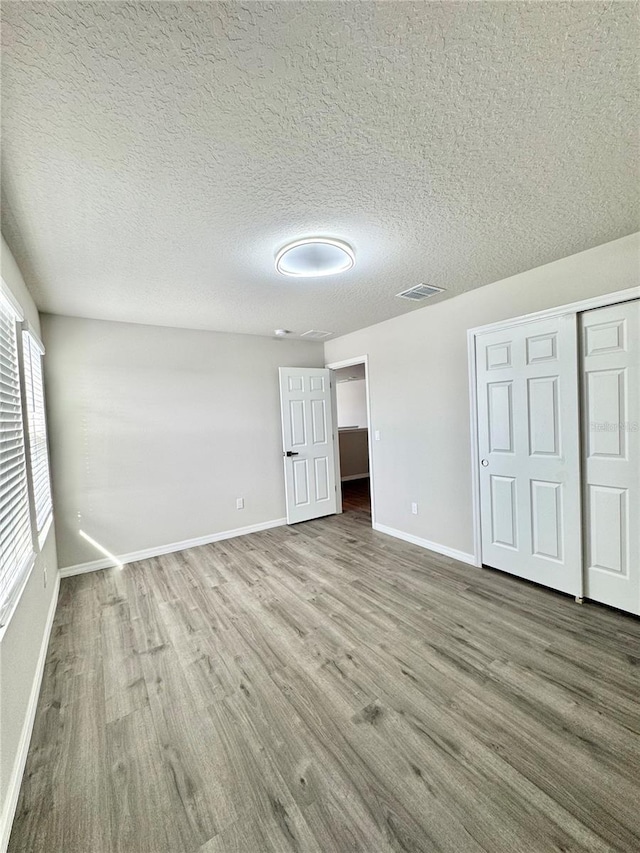 unfurnished bedroom featuring hardwood / wood-style floors, a closet, and a textured ceiling