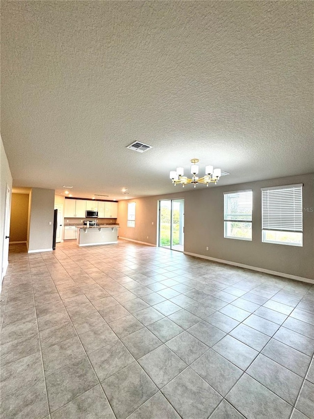 unfurnished living room with an inviting chandelier, light tile patterned floors, and a textured ceiling