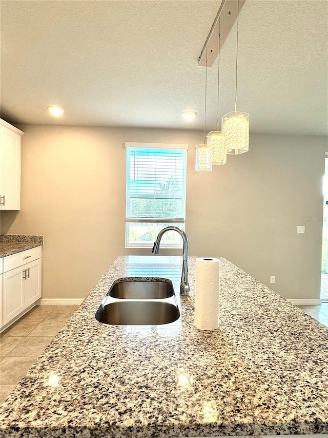 kitchen with stone countertops, pendant lighting, white cabinetry, sink, and light tile patterned floors