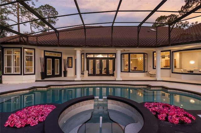 pool at dusk featuring a patio, an in ground hot tub, and a lanai