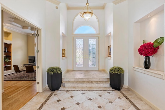 entrance foyer featuring light hardwood / wood-style flooring, a towering ceiling, ornamental molding, and french doors