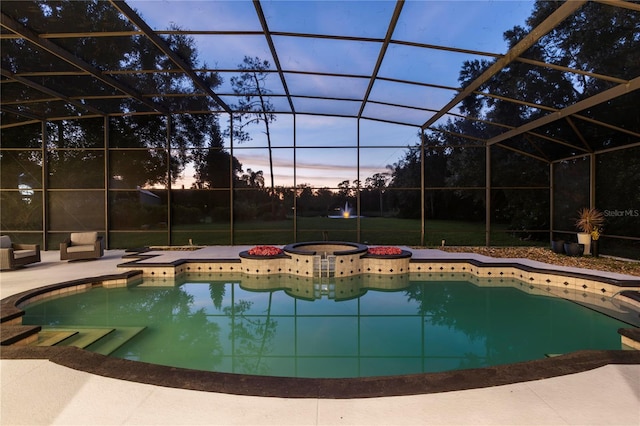 pool at dusk featuring glass enclosure, an in ground hot tub, and a patio area