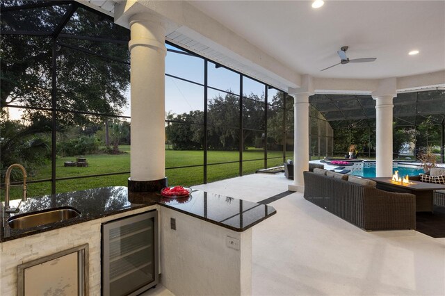 view of patio featuring glass enclosure, beverage cooler, ceiling fan, and sink