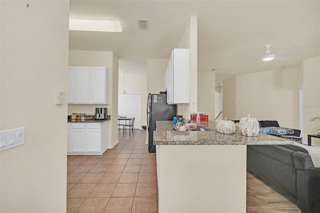 kitchen featuring white cabinetry, kitchen peninsula, light stone countertops, ceiling fan, and light tile patterned floors