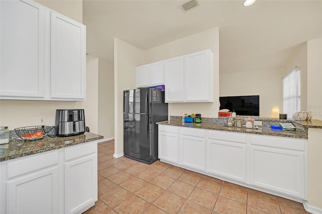 kitchen featuring dark stone counters, white cabinetry, black fridge, and light tile patterned floors