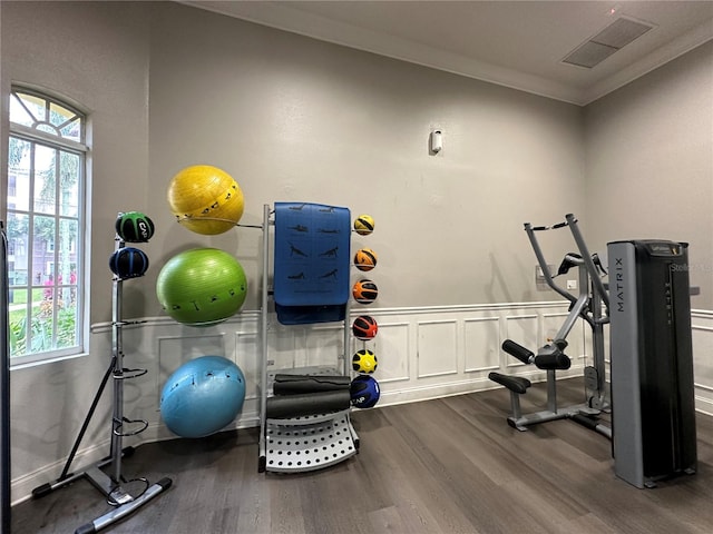 exercise room with wood finished floors, a wainscoted wall, visible vents, crown molding, and a decorative wall