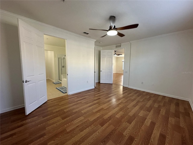 unfurnished bedroom featuring wood finished floors, baseboards, visible vents, ornamental molding, and ensuite bathroom