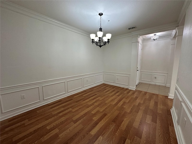 empty room featuring visible vents, wood finished floors, a chandelier, and crown molding