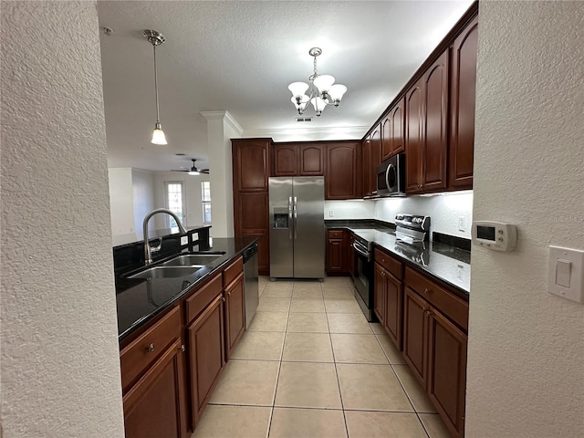 kitchen with light tile patterned floors, a sink, stainless steel appliances, decorative light fixtures, and a textured wall