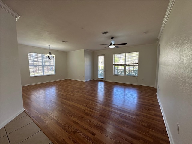 empty room featuring ceiling fan with notable chandelier, wood finished floors, visible vents, and ornamental molding