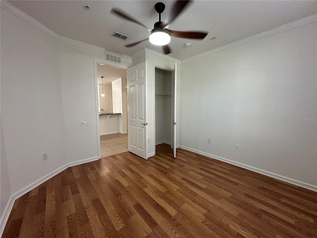 unfurnished bedroom featuring visible vents, baseboards, wood finished floors, and ornamental molding