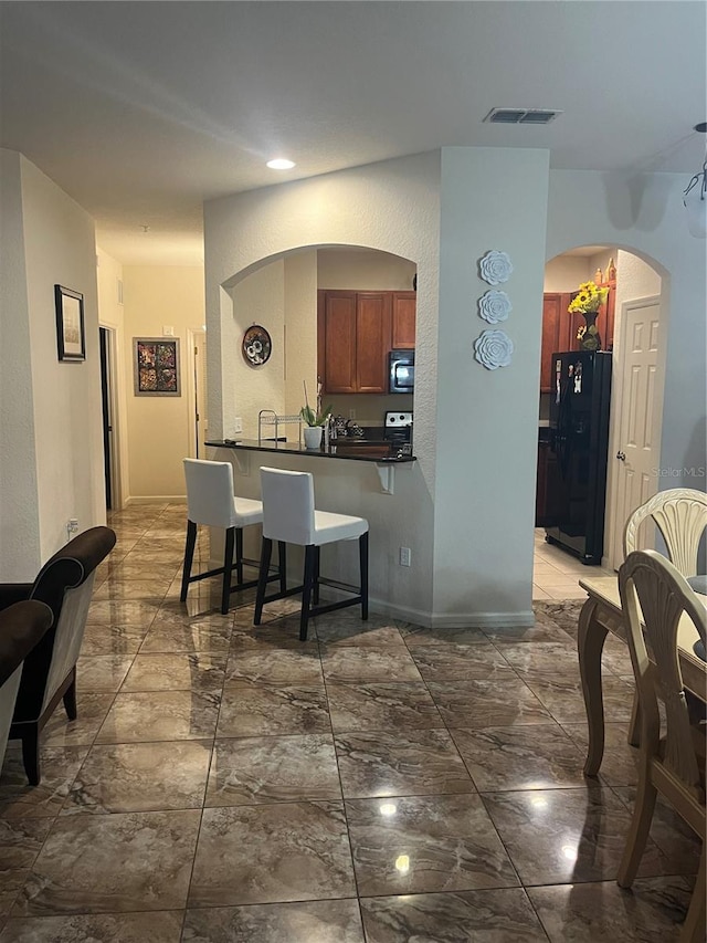 kitchen with kitchen peninsula, a breakfast bar, and black refrigerator