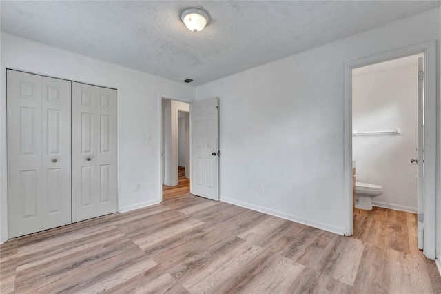 unfurnished bedroom featuring a textured ceiling, a closet, connected bathroom, and light hardwood / wood-style flooring