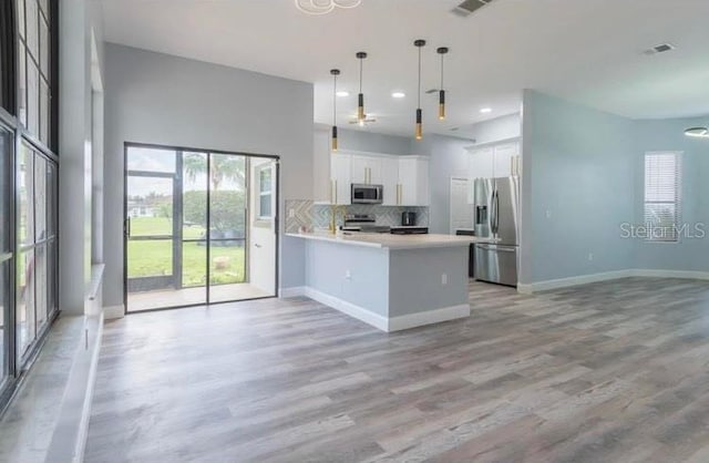 kitchen with appliances with stainless steel finishes, hanging light fixtures, light hardwood / wood-style floors, white cabinetry, and kitchen peninsula